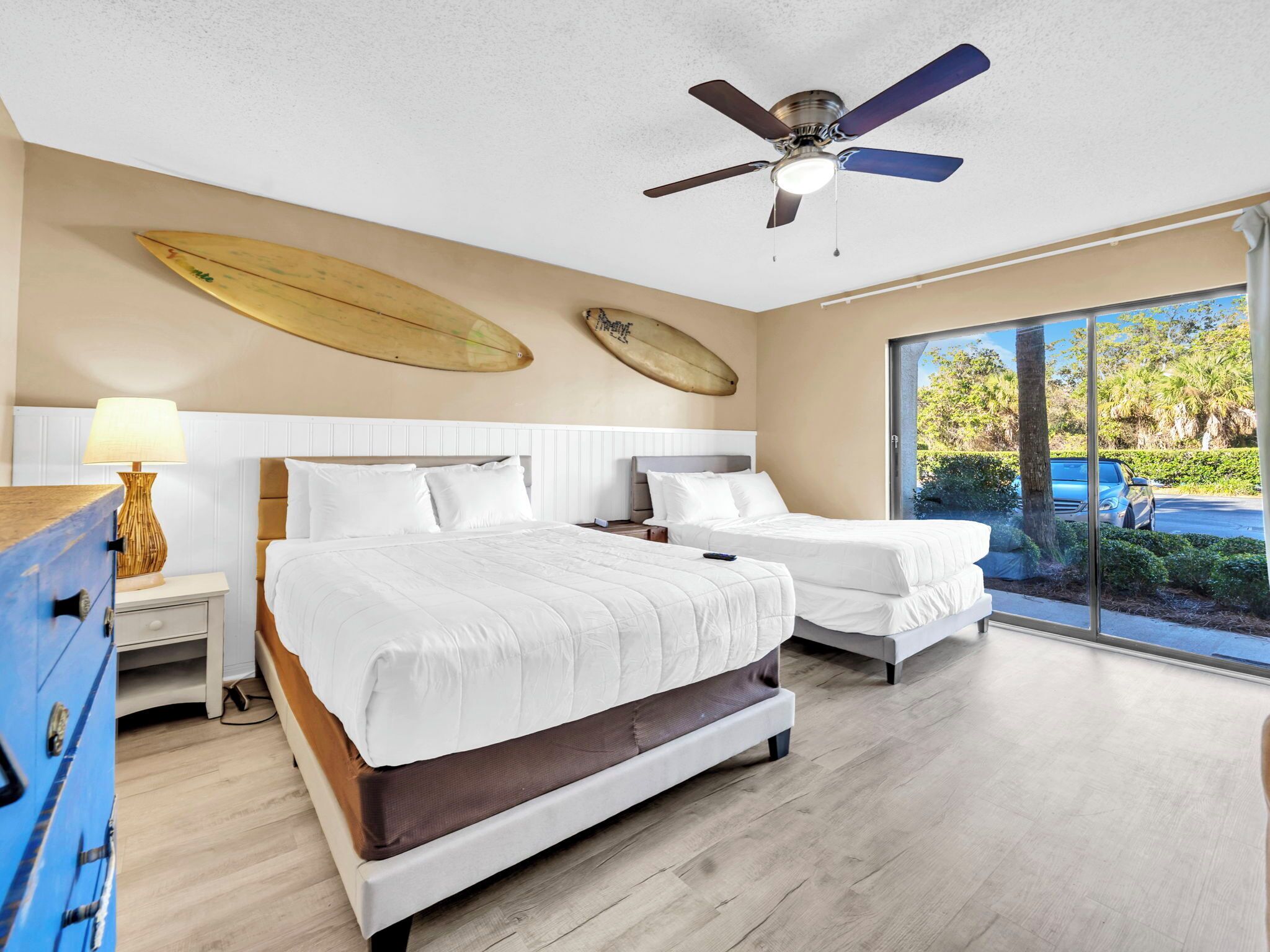 Un dormitorio con dos camas, un ventilador de techo y una tabla de surf en la pared.