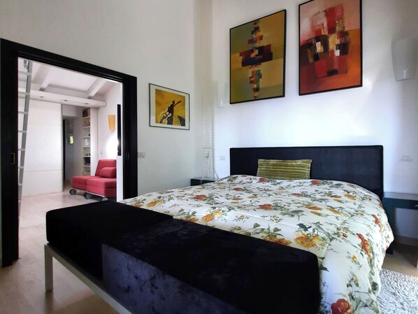 Un dormitorio con cama, un banco, una silla roja y dos cuadros en la pared.