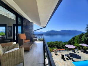 A balcony with wicker furniture, a pool, and a view of a lake and mountains.