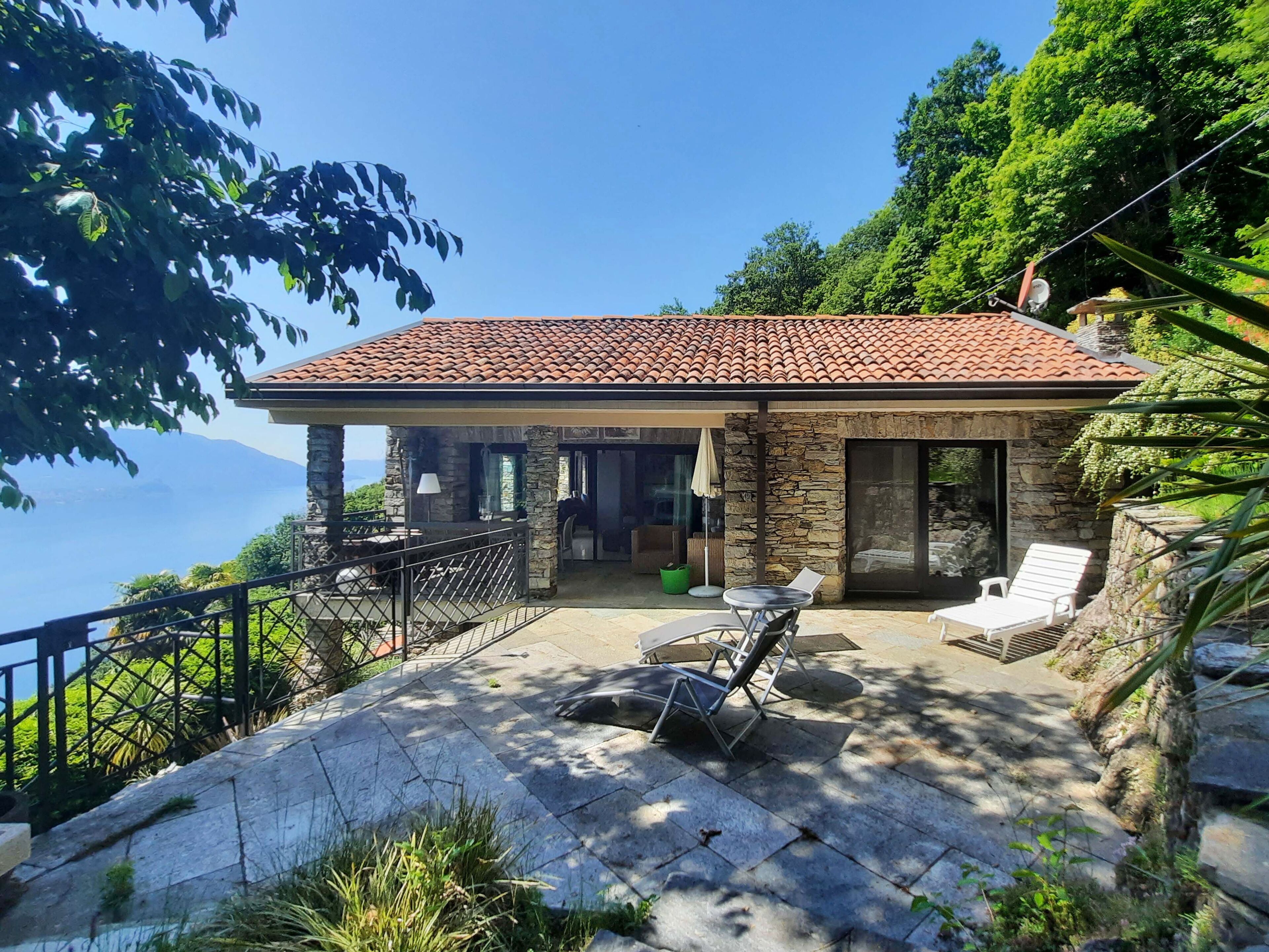 Ein Steinhaus mit Ziegeldach, einer Terrasse mit Stühlen und Blick auf das Meer.