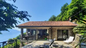 Una casa in pietra con tetto in tegole, un patio con sedie e vista sul mare.