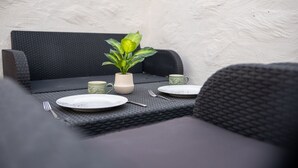 Zona pranzo con tavolo apparecchiato per due, piatti, posate e una pianta in vaso.