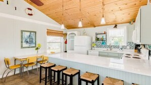 A modern kitchen with a large island, bar stools, and a wooden ceiling.