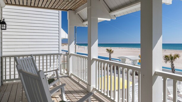 Een overdekt terras met witte hekwerk, een houten plafond en uitzicht op het strand.