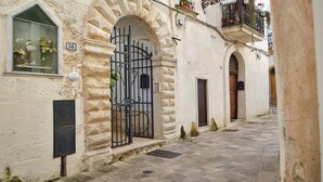 Une rue étroite avec un bâtiment en pierre, un portail en métal et une fenêtre ornée de plantes.