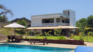 A swimming pool with lounge chairs, a covered seating area, and a two-story building with a balcony. - Beautiful double room with pool and kitchen, 850m to the Indian Ocean (Diani Beach)