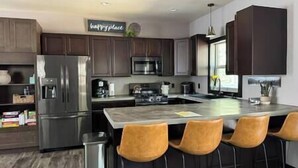 A modern kitchen with dark wood cabinets, stainless steel appliances, and a central island with bar stools. - Mile-high Pines Lodge (South Lawrence)