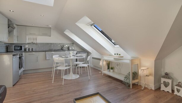 A modern kitchen with a dining area, featuring a skylight, white cabinetry, and a wooden floor. - Trinity House Apartment | Grampian Lettings (Aberdeen)
