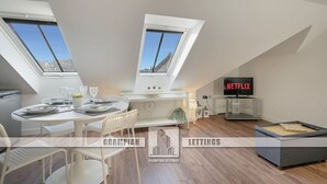 A modern loft apartment with skylights, a dining area, a living space with a TV, and a kitchenette. - Trinity House Apartment | Grampian Lettings (Aberdeen)