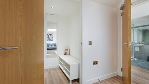 A modern interior with a wooden door, a white wall, and a visible bathroom with a shower and sink. - Trinity House Apartment | Grampian Lettings (Aberdeen)