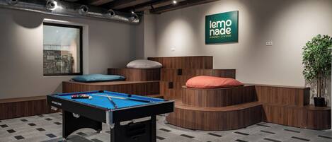 Une table de billard dans une pièce avec un banc en bois, un panneau fixé au mur et une plante en pot.