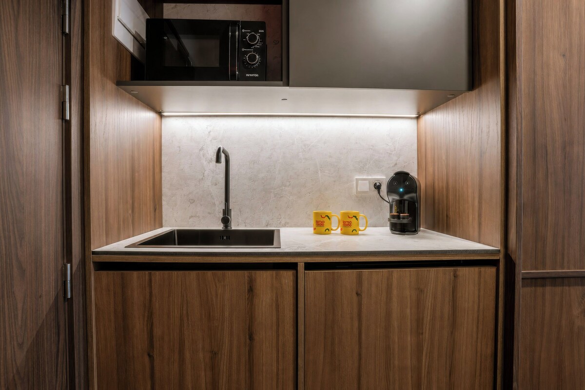Cocina compacta con microondas integrado, un lavamanos con grifo moderno y una cafetera sobre la encimera.