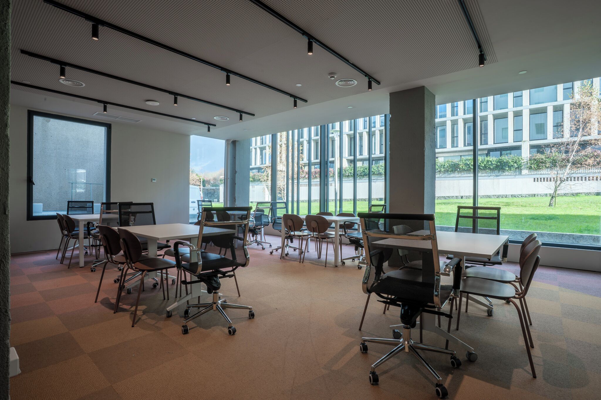 A modern conference room with large windows, multiple tables, and chairs.