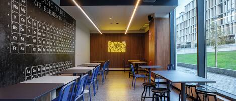 A modern cafe with a periodic table mural, wooden accents, and large windows offering a view of the outside.