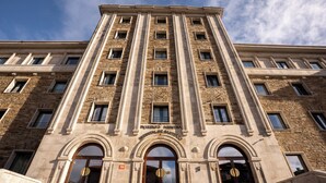 Un edificio de varios pisos con estilo arquitectónico clásico, que presenta una entrada central con arcos y un letrero grande y destacado sobre la entrada.