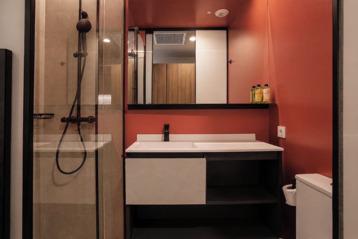 A modern bathroom with a glass-enclosed shower, a white sink with a black cabinet, and a mirror above the sink.