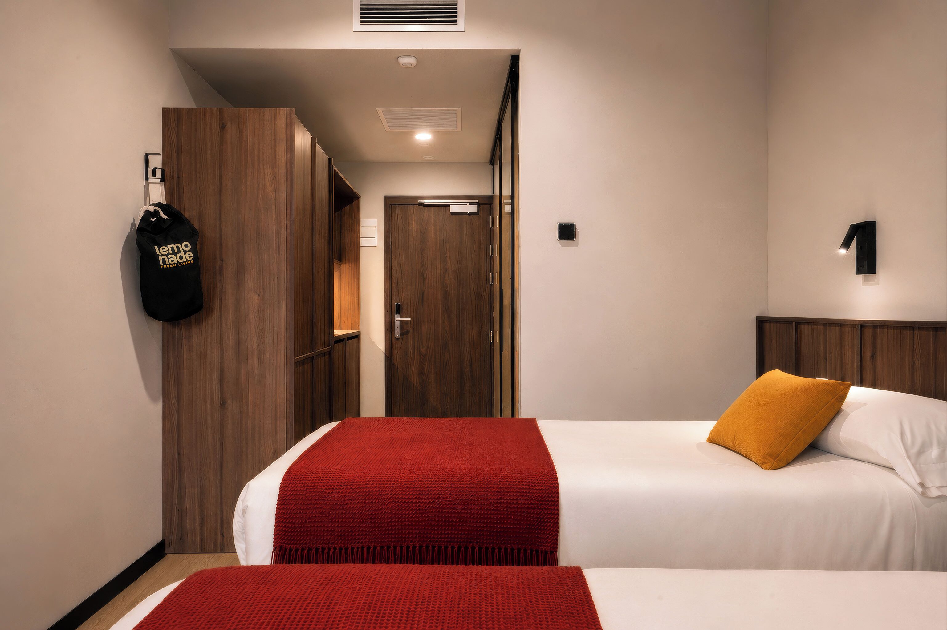 Ein Hotelzimmer mit zwei Betten, einer roten Decke, einem Sandsack und einem Holzschrank.