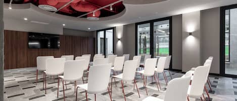 Ein moderner Konferenzraum mit weißen Stühlen und Tischen, großen Fenstern und einer roten Decke mit freiliegenden Rohren.