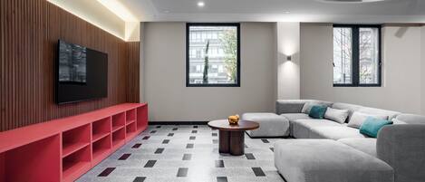 A modern living room with a flat-screen TV, a red bench, a grey sectional sofa, and a patterned floor.