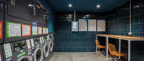 A laundromat with multiple washing machines, a table, and chairs.