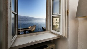Une vue depuis une fenêtre donnant sur une étendue d’eau calme où sont amarrés des bateaux, avec un ciel dégagé et des montagnes à l’horizon.