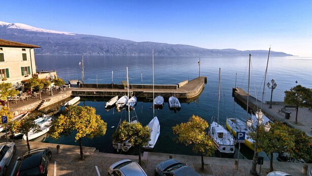 Un port de plaisance avec des bateaux amarrés, un bâtiment doté d’un balcon et une vue dégagée sur l’eau et les montagnes en arrière-plan.