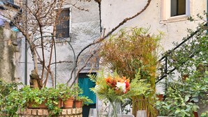 Un espace de restauration en plein air avec une table dressée pour deux personnes, entouré de plantes en pot et d’un mur de pierres rustiques.