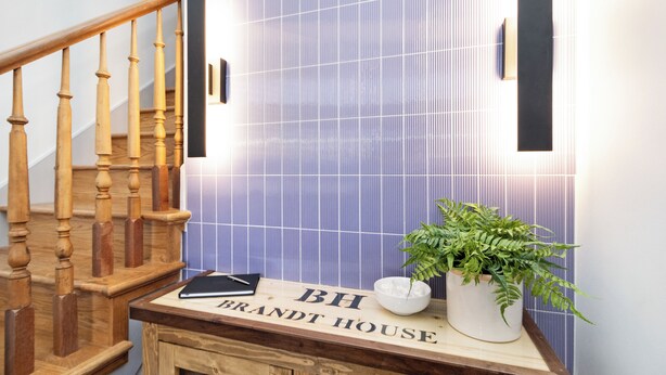 A staircase with wooden balusters, a sign reading "BH BRANDT HOUSE," a potted plant, and a bowl of ice. - Brandt House (Alma)