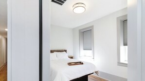 A bedroom with a bed, a window with blinds, a ceiling light, and a wooden floor. - Brandt House (Alma)