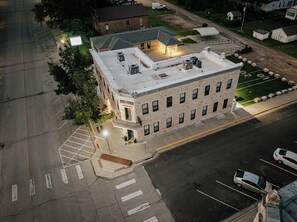 A multi-story building with a brick facade, a flat roof, and a parking lot with marked spaces. - Brandt House (Alma)
