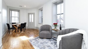 A spacious room with hardwood flooring, a dining area with a round table and chairs, a grey armchair, and a sofa with a white throw. - Brandt House (Alma)