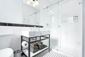 Un baño moderno con lavamanos blanco, encimera de mármol y cabina de ducha de vidrio.