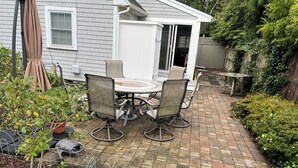 A patio with a round table and four chairs, surrounded by a brick pathway and greenery.