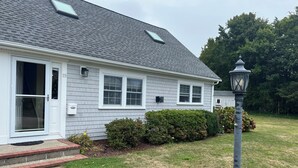 A single-story house with a grey shingle roof, white siding, and a front door with glass panels.