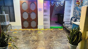 A room with a marble floor, a wooden door with a mesh design, a sofa, and potted plants. - Divya Darshan Stay (Faizabad)
