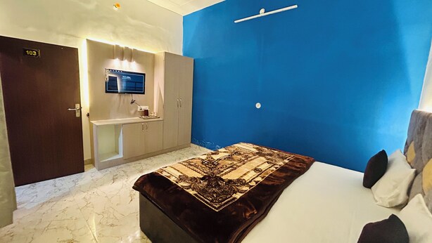 A hotel room with a bed, a desk with a computer, a mirror, and a blue accent wall.