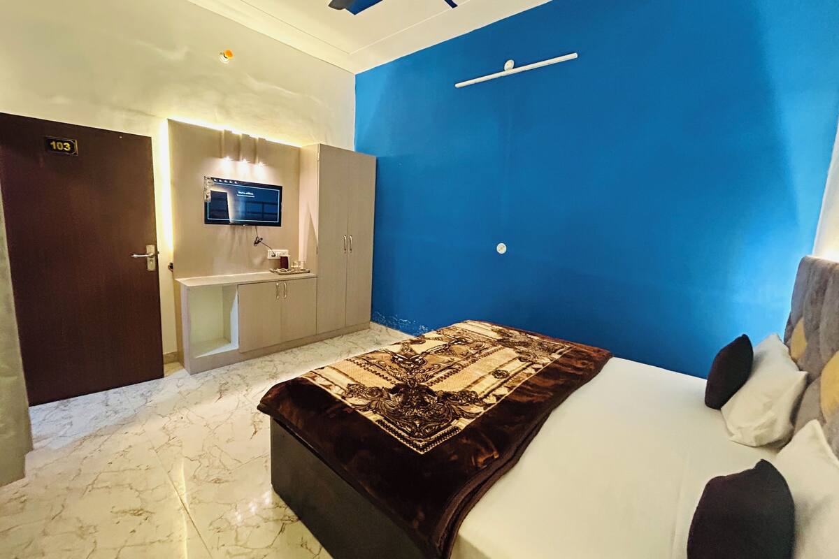 Une chambre d’hôtel avec un lit, un bureau avec un ordinateur, un miroir et un mur d’accent bleu.