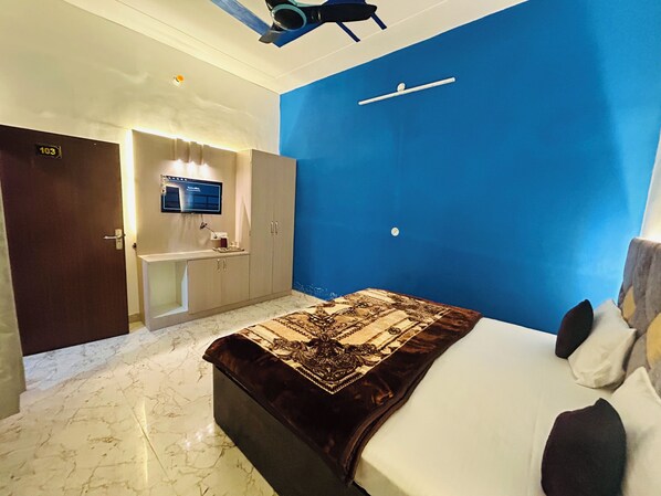 Una camera d'albergo con un letto, una scrivania con un computer, uno specchio e una parete azzurra.