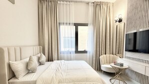 Une chambre d’hôtel moderne avec un grand lit, un téléviseur fixé au mur et une petite table ronde.