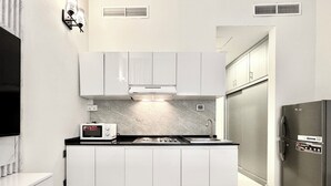 Une cuisine de taille réduite avec des meubles blancs, un four à micro-ondes encastré, une cuisinière et un réfrigérateur.