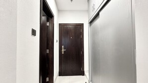 Un couloir étroit, avec une porte en bois sombre au fond, des murs blancs et un sol carrelé.