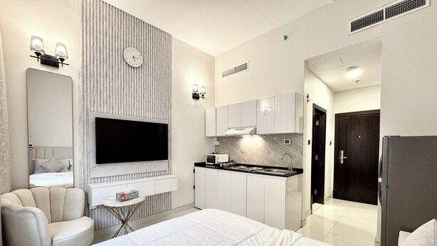 Une chambre d’hôtel moderne dotée d’un grand lit, d’un téléviseur fixé au mur, d’un petit coin cuisine et d’un espace salon séparé avec une chaise et une table.