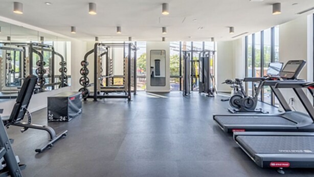 Una palestra moderna con diverse attrezzature per l'allenamento, tra cui tapis roulant e macchinari per pesi, e ampie finestre che offrono luce naturale.