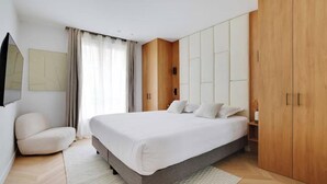 Un dormitorio moderno con una cama grande, un armario de madera y una pequeña zona de estar.