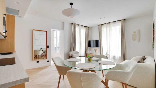 Una sala de estar moderna con una mesa de comedor de vidrio rodeada de sillas, un sofá y un televisor.