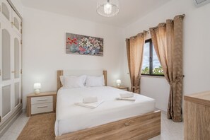A neatly arranged bedroom with a large bed, bedside tables, a painting, and a window with curtains. - Salicos Benagil Pool Villa (Lagoa)