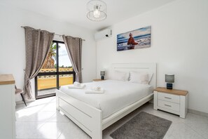 A bedroom with a bed, bedside tables, a nightstand, a window with curtains, an air conditioning unit, and a painting on the wall. - Salicos Benagil Pool Villa (Lagoa)