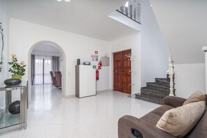 Een ruime woonkamer met een bank, een eettafel met stoelen, een trap en een deur.