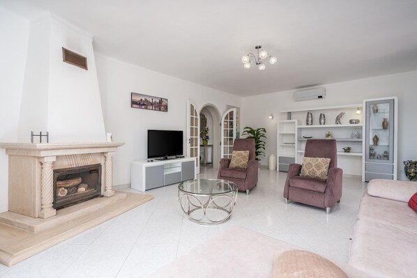 Een moderne woonkamer met een open haard, een televisie, een glazen salontafel en twee fauteuils.