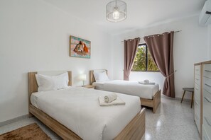 A hotel room with two beds, a wooden headboard, a painting on the wall, a window with curtains, and a wardrobe. - Salicos Benagil Pool Villa (Lagoa)